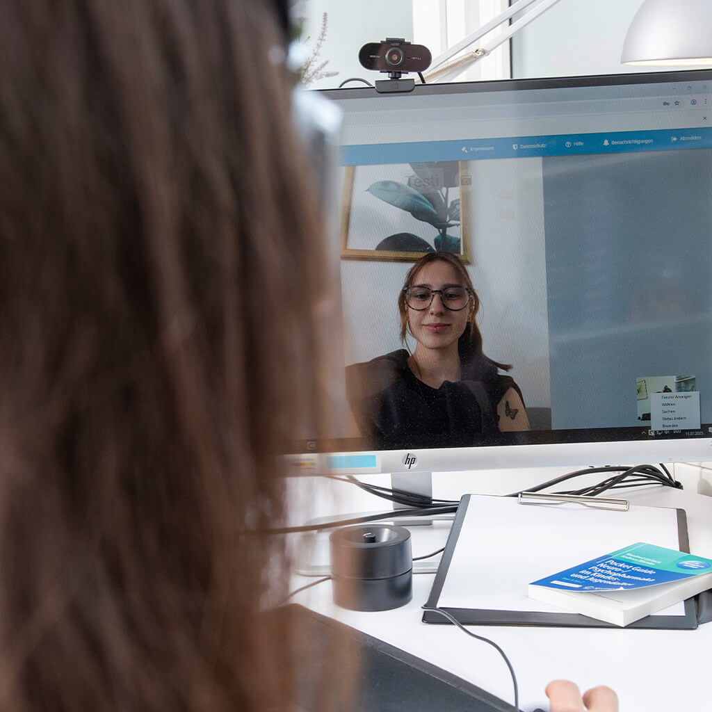 Ärztin führt eine Videosprechstunde durch, mit Monitor und Webcam im Sprechzimmer.